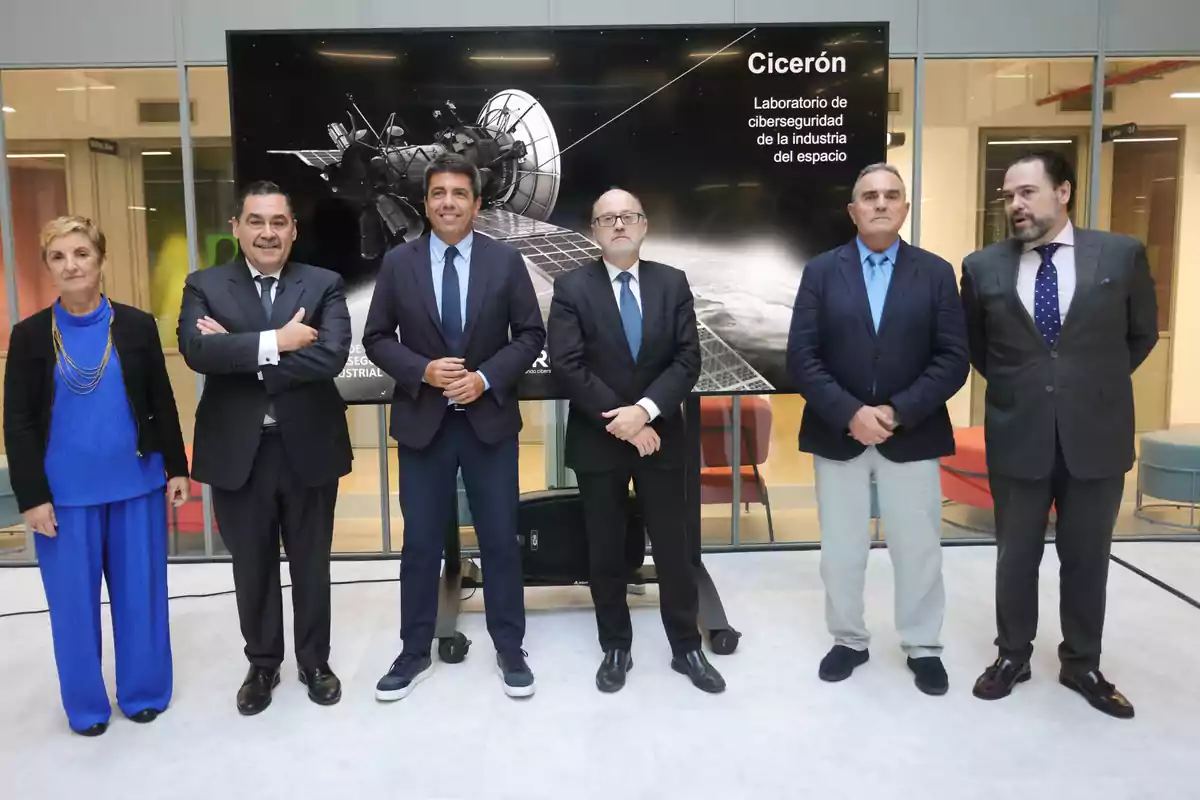 Seis personas posan de pie frente a una pantalla que muestra un satélite y el texto Cicerón Laboratorio de ciberseguridad de la industria del espacio, todos vestidos de manera formal en un entorno moderno y profesional. Seis personas posan de pie frente a una pantalla que muestra un satélite y el texto Cicerón Laboratorio de ciberseguridad de la industria del espacio, todos vestidos de manera formal en un entorno moderno y profesional.