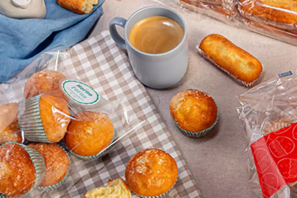 Taza de café junto a magdalenas y bizcochos sobre un mantel a cuadros Taza de café junto a magdalenas y bizcochos sobre un mantel a cuadros