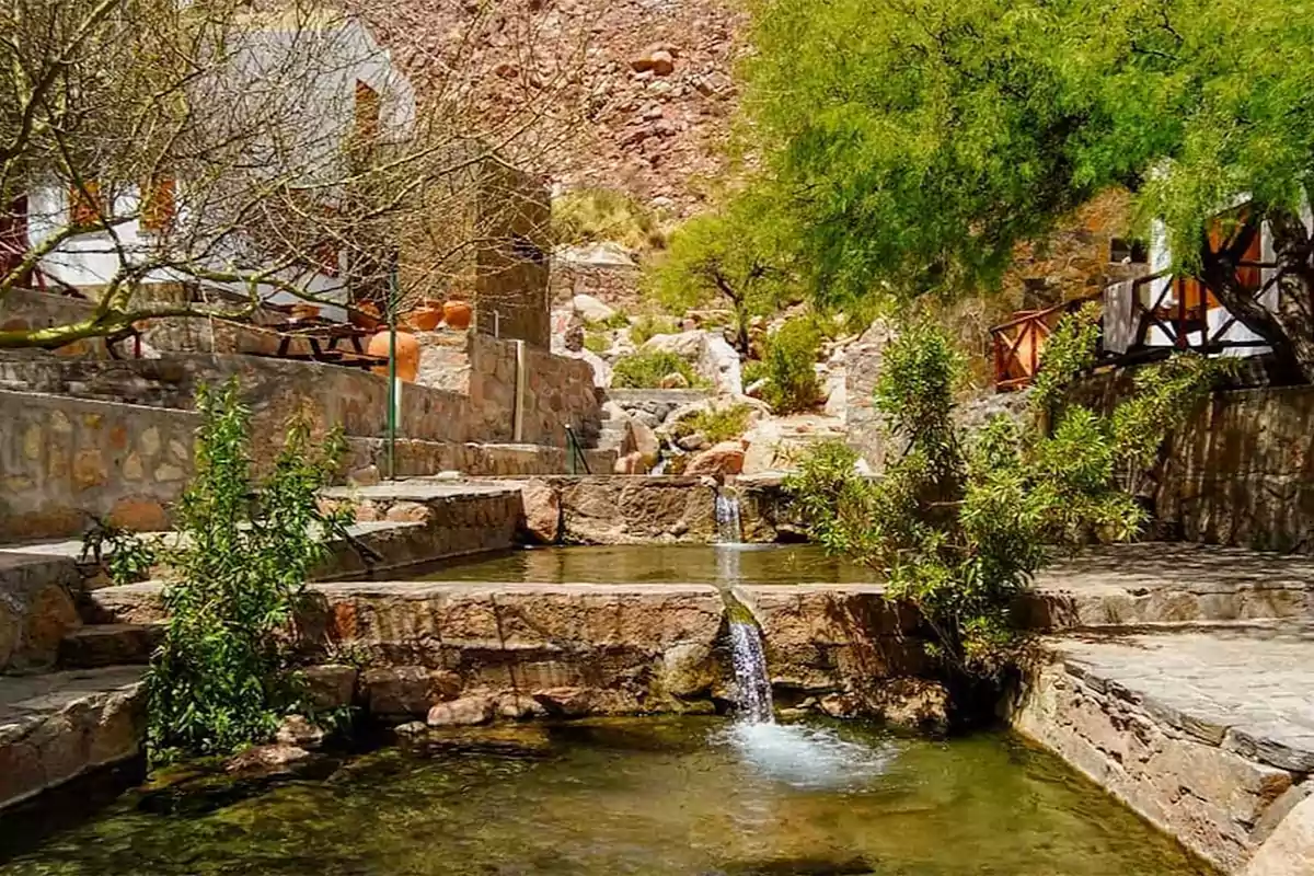 Piscina natural de aguas termales rodeada de vegetación y construcciones de piedra en un entorno montañoso Piscina natural de aguas termales rodeada de vegetación y construcciones de piedra en un entorno montañoso