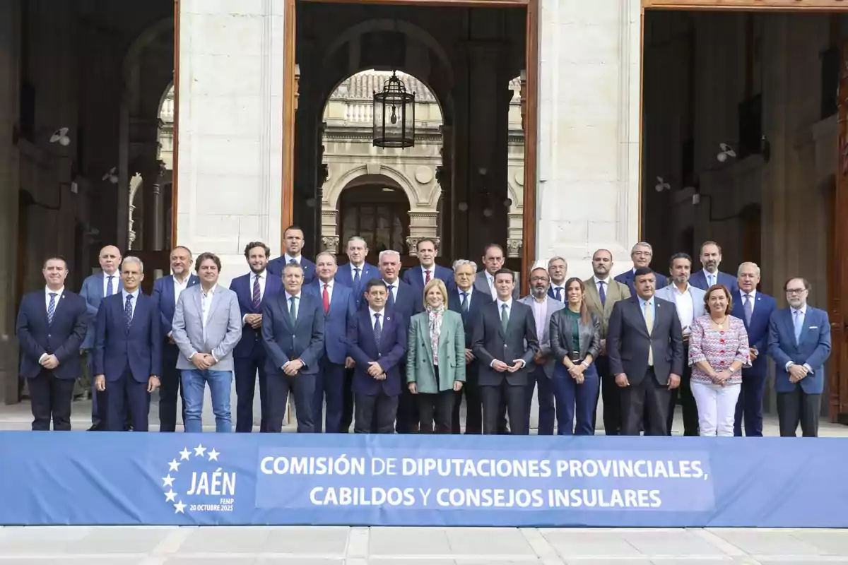 Grupo de personas posando frente a un edificio histórico junto a un cartel que indica una reunión de la Comisión de Diputaciones Provinciales, Cabildos y Consejos Insulares en Jaén