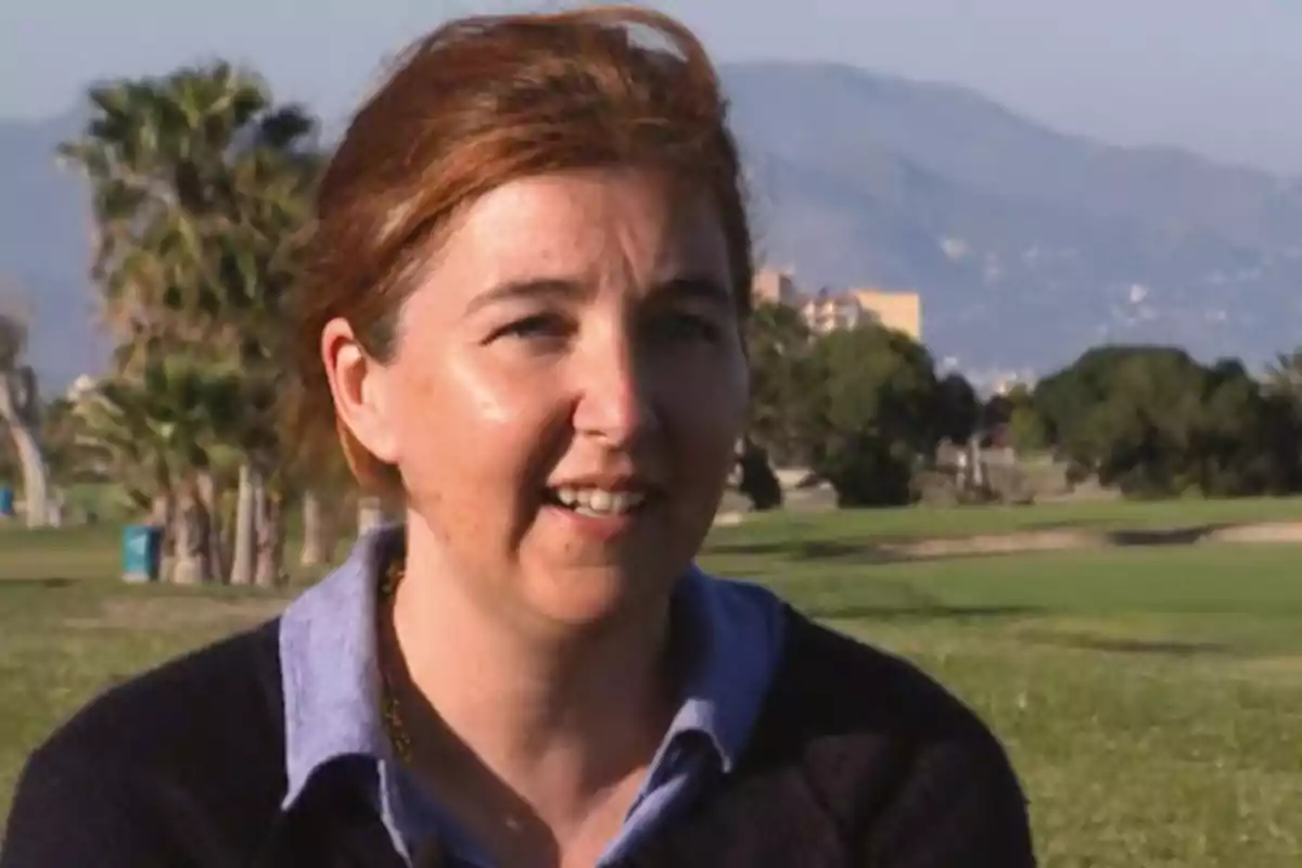 Mujer de cabello castaño claro sonriente al aire libre con árboles y montañas al fondo en un día soleado