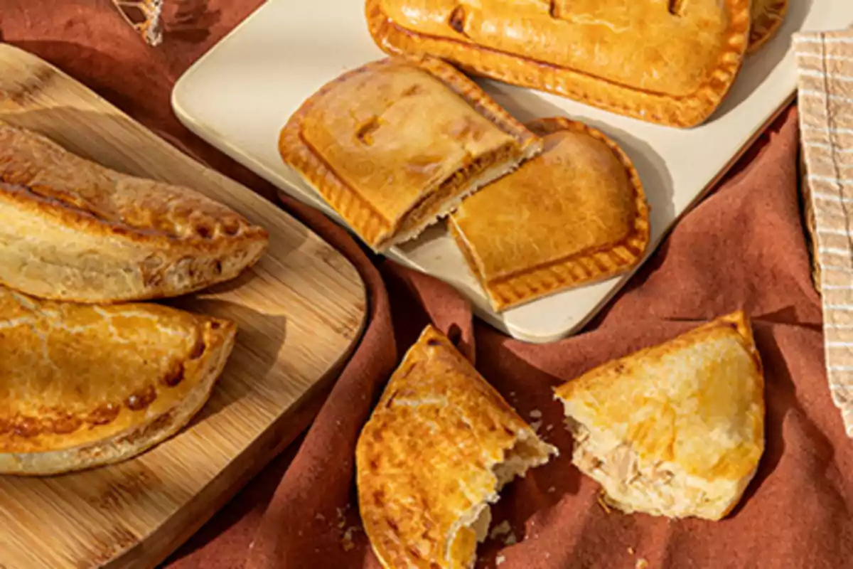 Empanadas y pasteles dorados sobre tablas de madera y tela marrón, algunos partidos mostrando su relleno