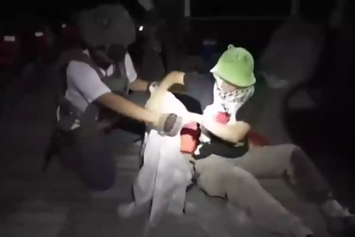 Persona con casco y mascarilla forcejeando con otra persona que lleva un sombrero verde y un pañuelo en el rostro en un ambiente oscuro Persona con casco y mascarilla forcejeando con otra persona que lleva un sombrero verde y un pañuelo en el rostro en un ambiente oscuro