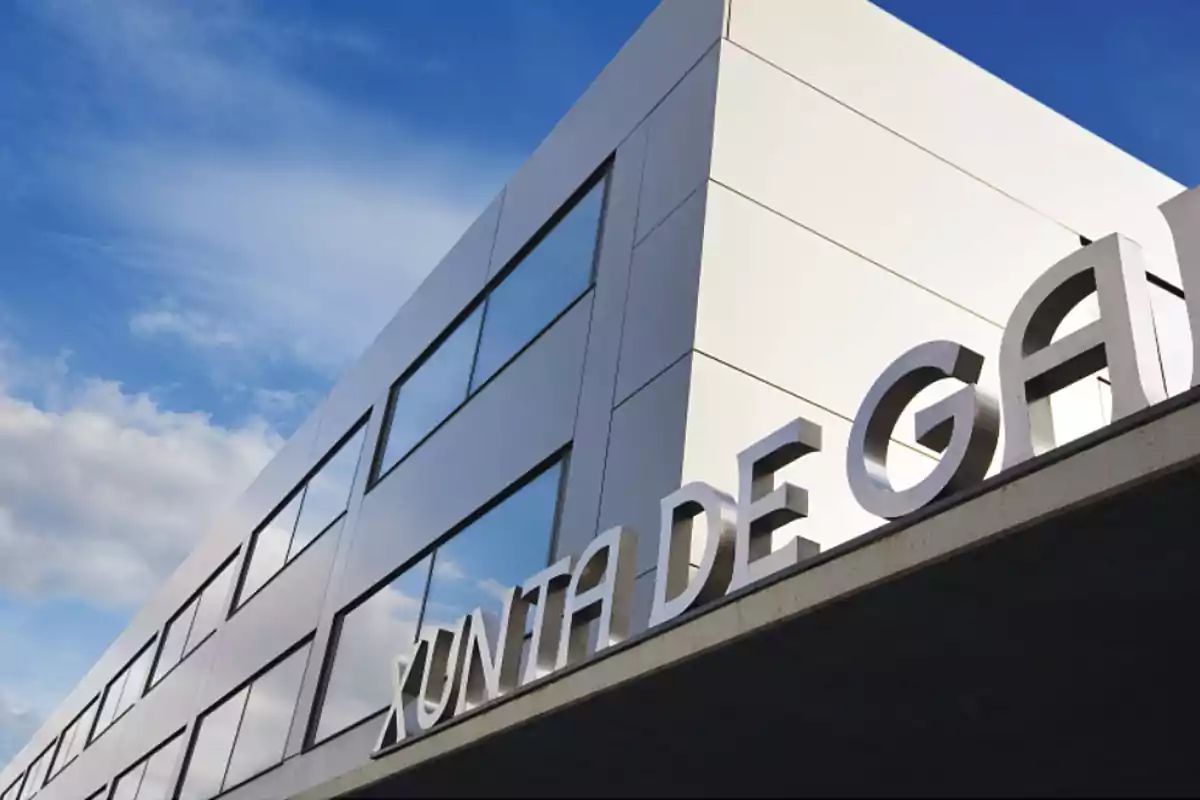 Edificio moderno con grandes ventanales y letras plateadas que dicen Xunta de Galicia bajo un cielo azul con algunas nubes