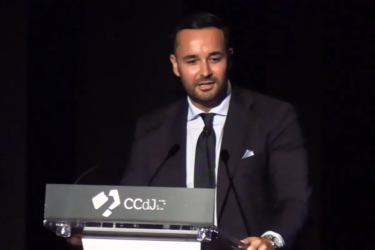 Hombre de traje oscuro hablando en un podio con el logo de CCdJ en un fondo negro