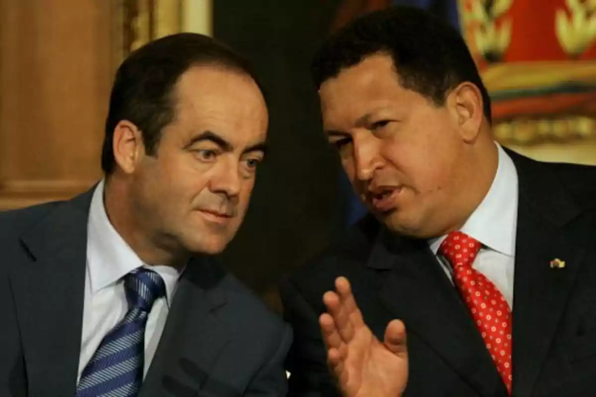 Dos hombres de traje conversan en un ambiente formal uno de ellos gesticula con la mano mientras habla