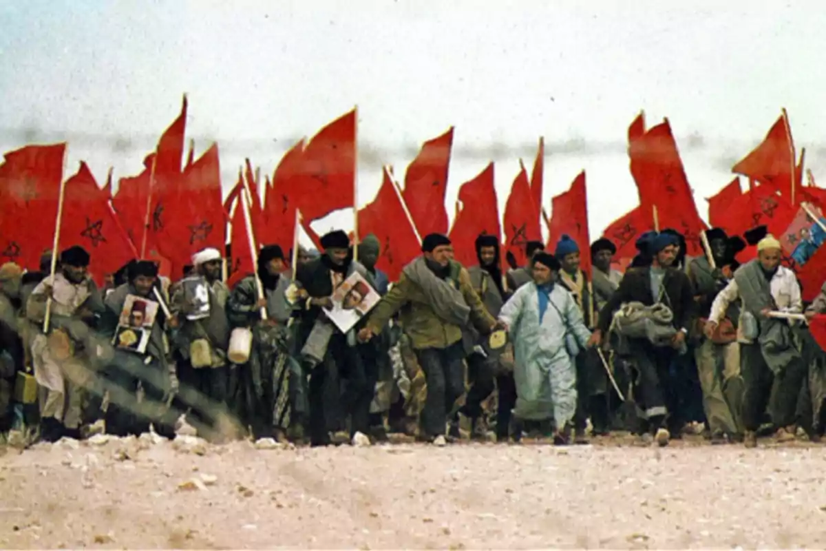 Multitud de personas marchando en el desierto con banderas rojas de Marruecos y retratos en las manos