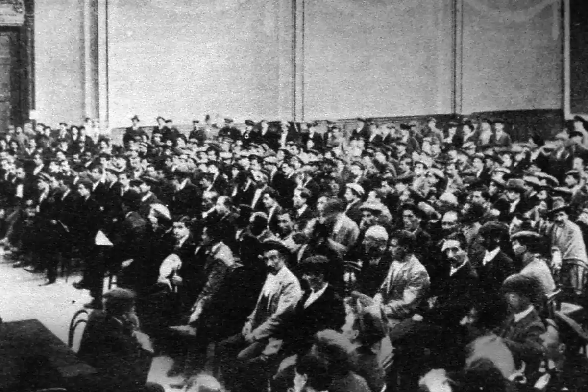 Fotografía antigua en blanco y negro de un auditorio lleno de personas sentadas prestando atención a un evento o conferencia