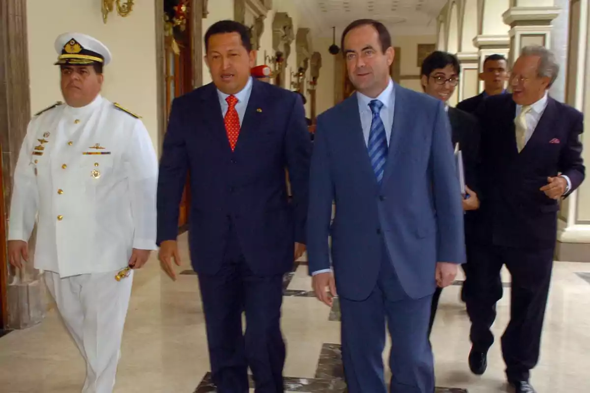 Un grupo de hombres vestidos de traje y uno con uniforme militar caminan por un pasillo elegante dentro de un edificio gubernamental Un grupo de hombres vestidos de traje y uno con uniforme militar caminan por un pasillo elegante dentro de un edificio gubernamental