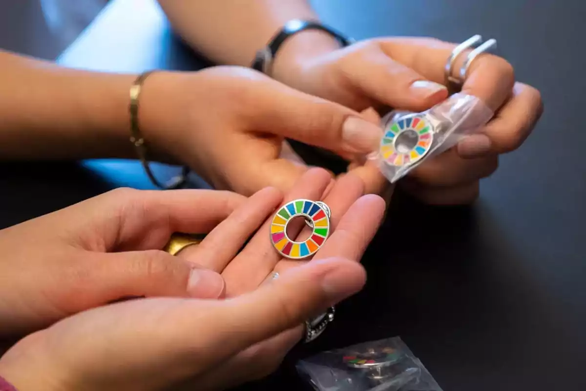 Manos sosteniendo pines circulares con colores representativos de los Objetivos de Desarrollo Sostenible sobre una mesa negra