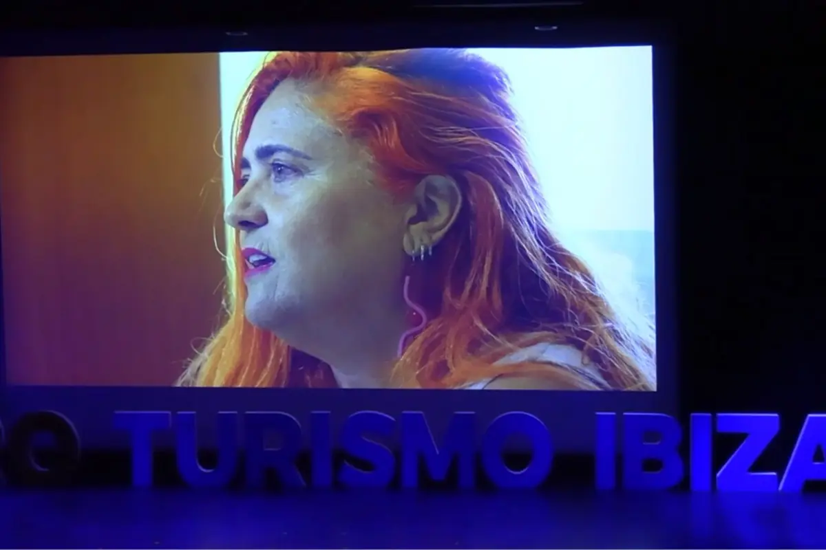 Mujer de cabello naranja proyectada en una pantalla durante un evento con letras grandes que dicen TURISMO IBIZA en el escenario