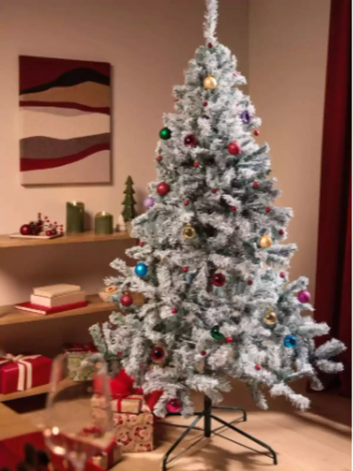 Árbol de Navidad nevado decorado con esferas de colores en una sala con regalos y adornos navideños