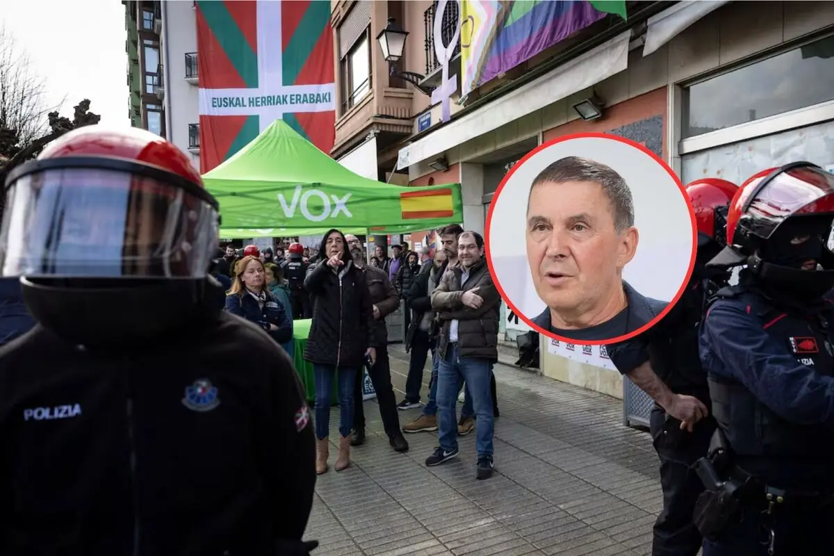 Policías con casco y personas manifestándose frente a una carpa verde de VOX en una calle, con una gran bandera vasca y otra multicolor colgadas en los edificios y un retrato de un hombre enmarcado en un círculo rojo sobrepuesto en la imagen