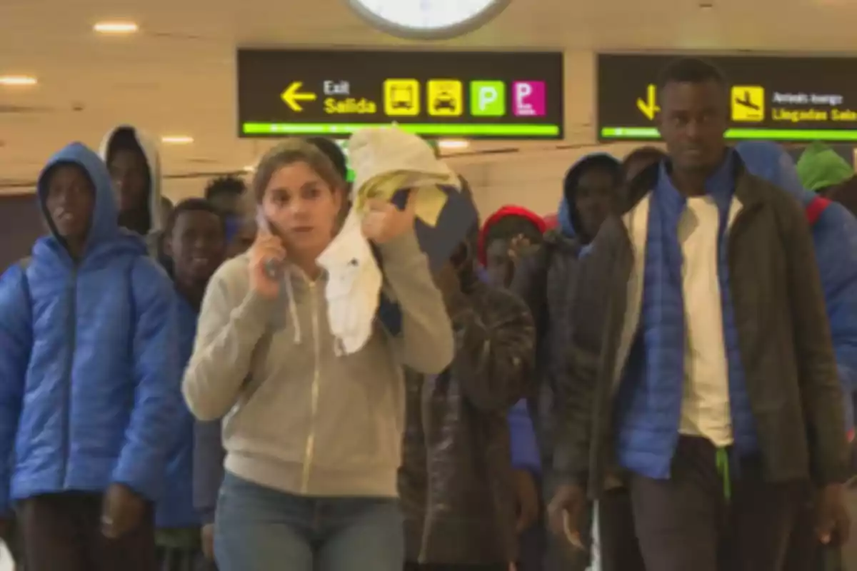 Grupo de personas caminando en un aeropuerto con señales de salida y estacionamiento al fondo