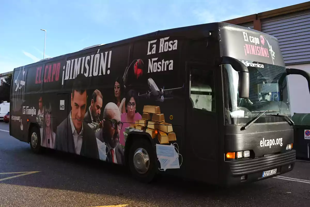 Autobús negro con imágenes de políticos, lingotes de oro, mascarillas, un avión y mensajes de protesta en los laterales