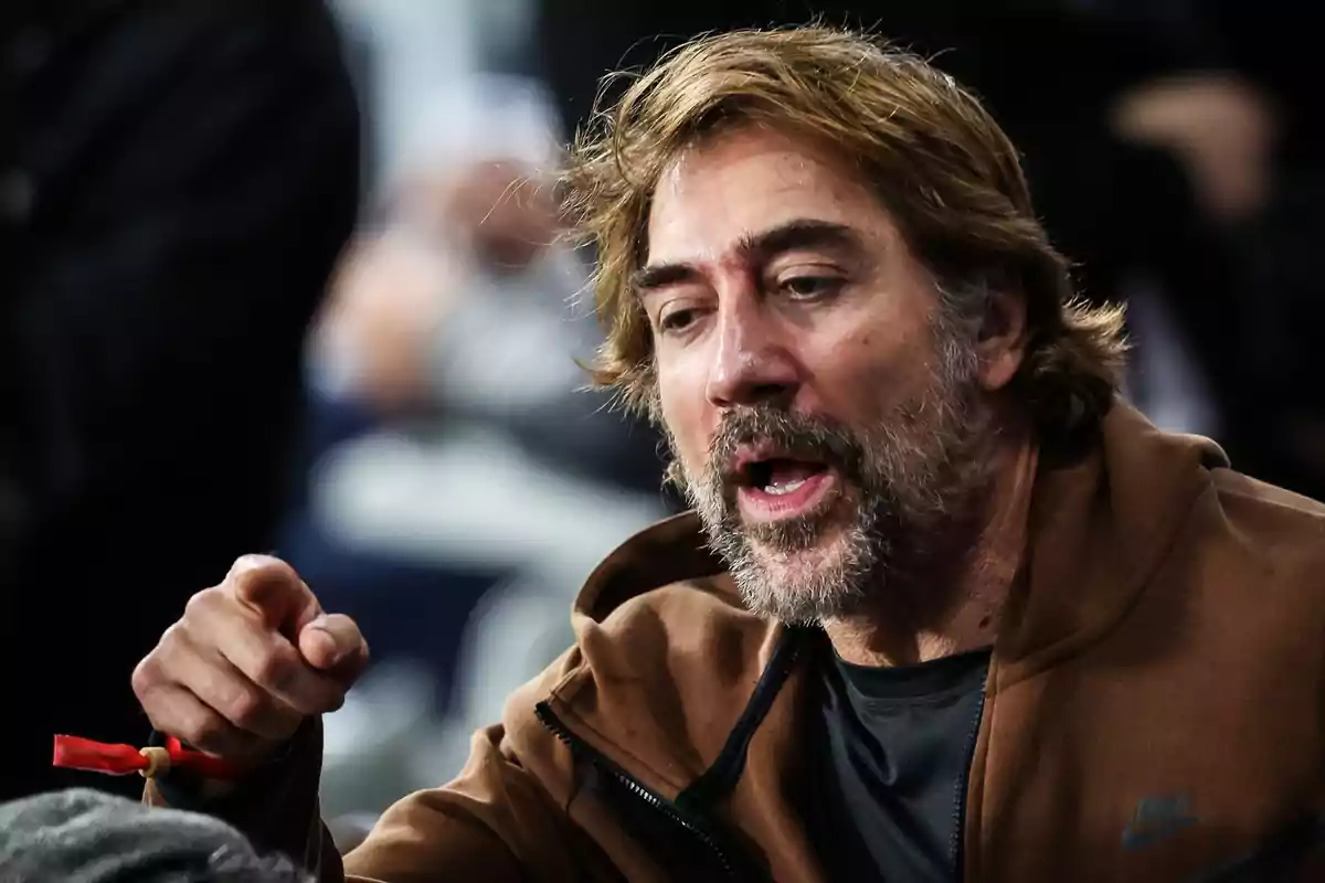 Hombre de cabello castaño y barba hablando y señalando con el dedo mientras viste una chaqueta marrón Hombre de cabello castaño y barba hablando y señalando con el dedo mientras viste una chaqueta marrón