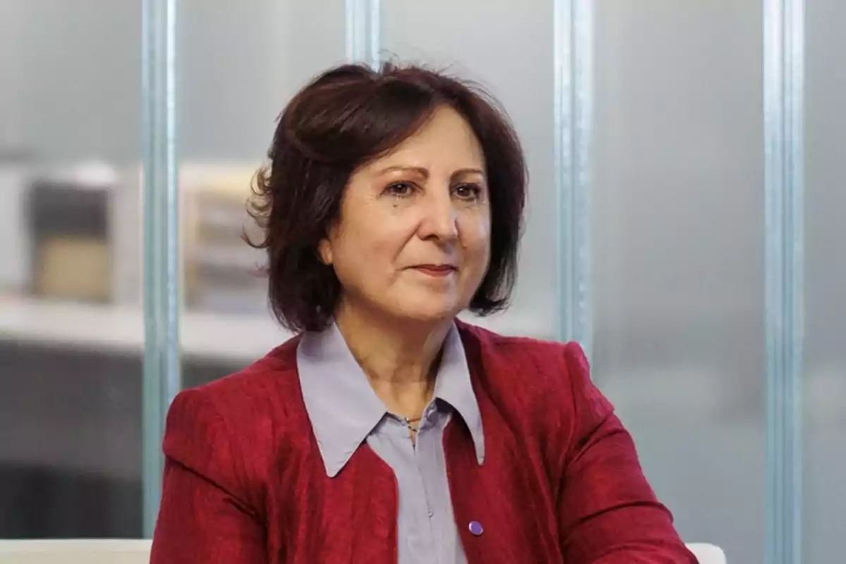 Mujer de cabello castaño y corto con chaqueta roja y blusa clara sentada en un entorno de oficina