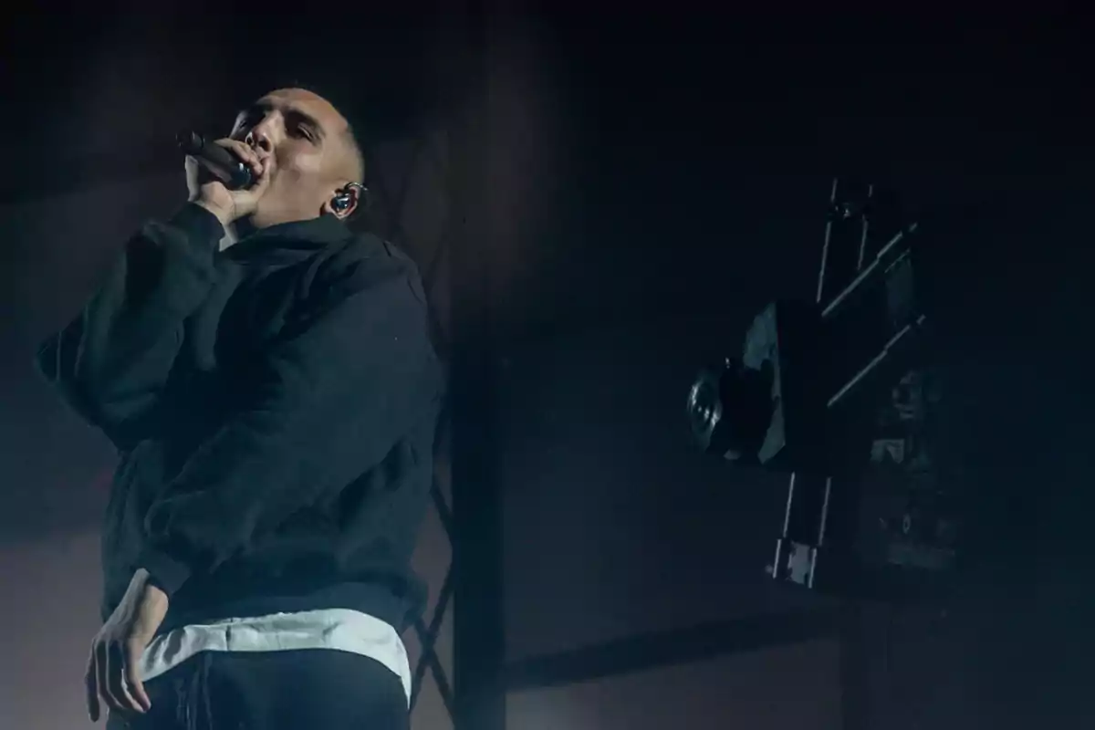 Persona cantando en el escenario con micrófono en mano y una cámara grabando a un lado