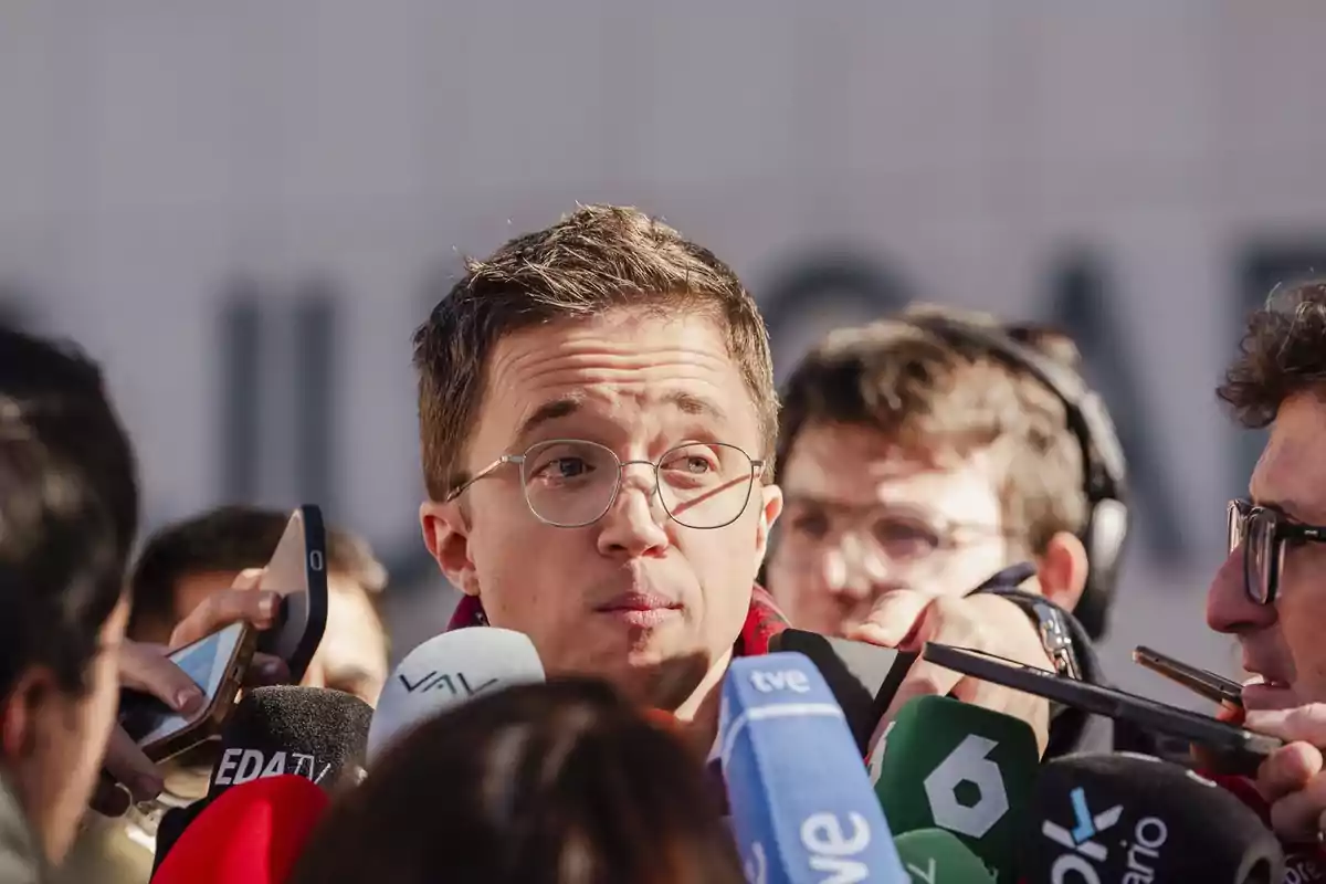 Un hombre con gafas rodeado de micrófonos y periodistas mientras responde preguntas frente a las cámaras