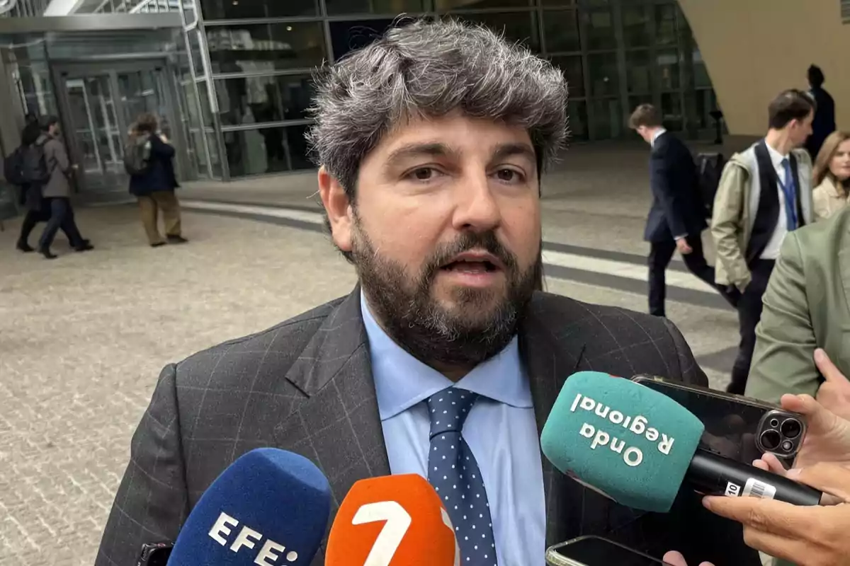 Un hombre con barba y cabello canoso da declaraciones a la prensa frente a un edificio mientras varios micrófonos y teléfonos móviles lo rodean. Un hombre con barba y cabello canoso da declaraciones a la prensa frente a un edificio mientras varios micrófonos y teléfonos móviles lo rodean.