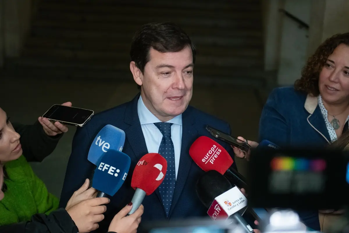 Un hombre con traje y corbata responde preguntas de varios periodistas que sostienen micrófonos y grabadoras frente a él.