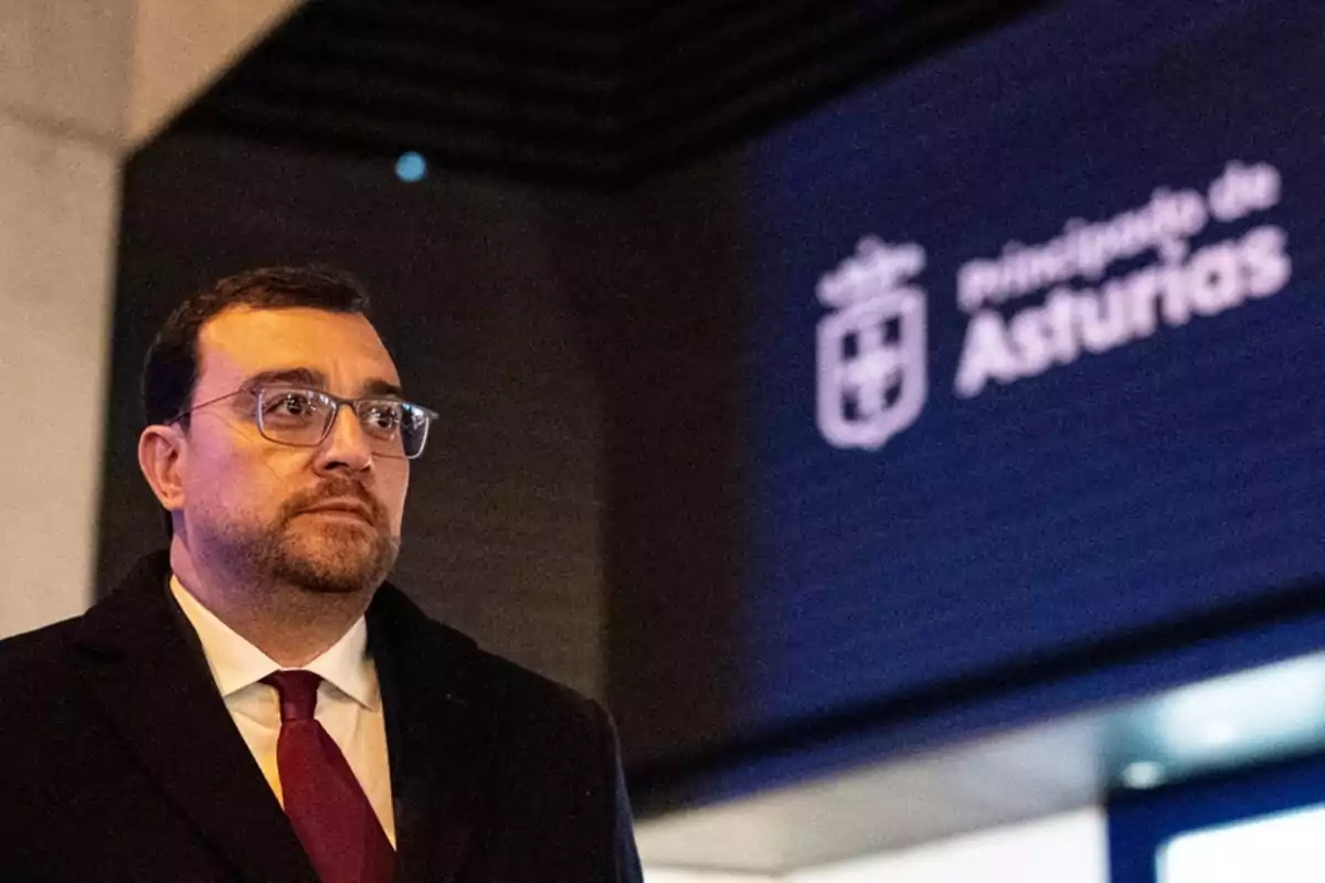 Hombre con gafas y corbata roja de pie frente a un letrero iluminado que dice Principado de Asturias Hombre con gafas y corbata roja de pie frente a un letrero iluminado que dice Principado de Asturias