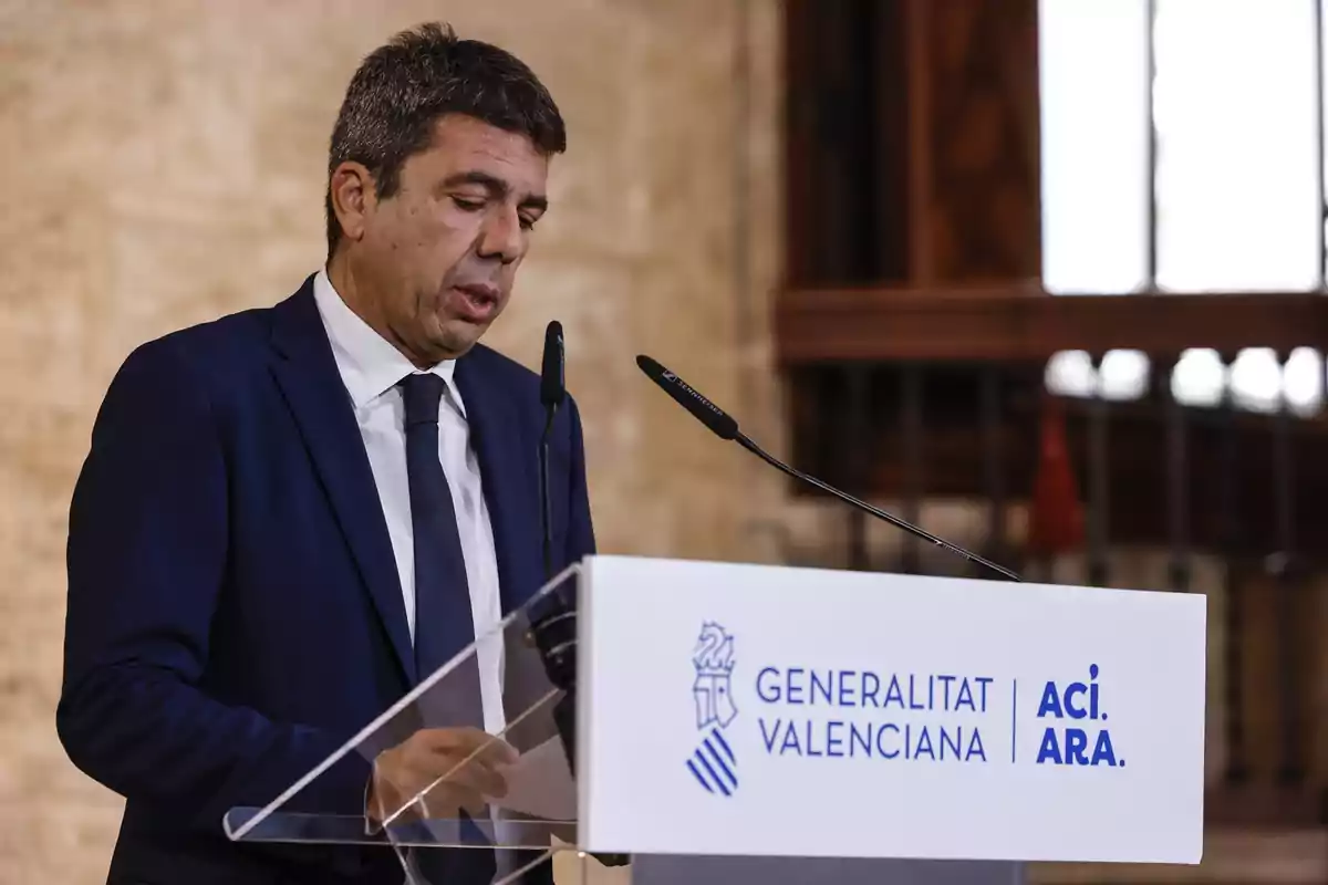 Hombre con traje azul hablando en un atril con el logo de la Generalitat Valenciana en un interior elegante Hombre con traje azul hablando en un atril con el logo de la Generalitat Valenciana en un interior elegante