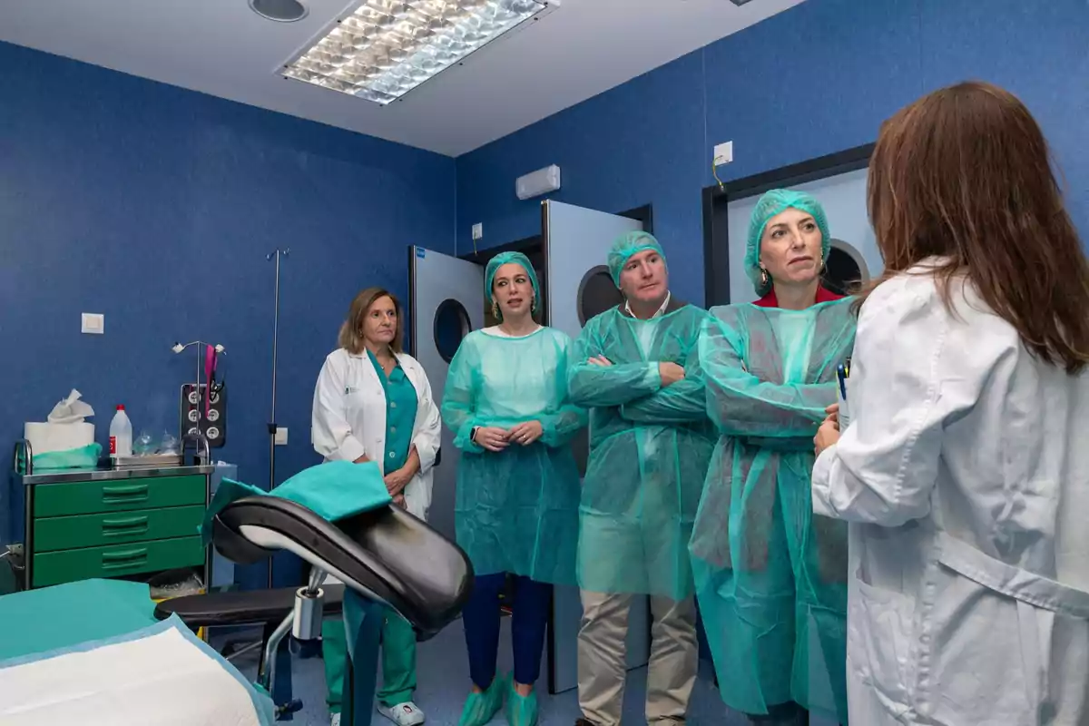 Varias personas con batas y gorros quirúrgicos escuchan a una profesional de la salud en una sala médica equipada Varias personas con batas y gorros quirúrgicos escuchan a una profesional de la salud en una sala médica equipada