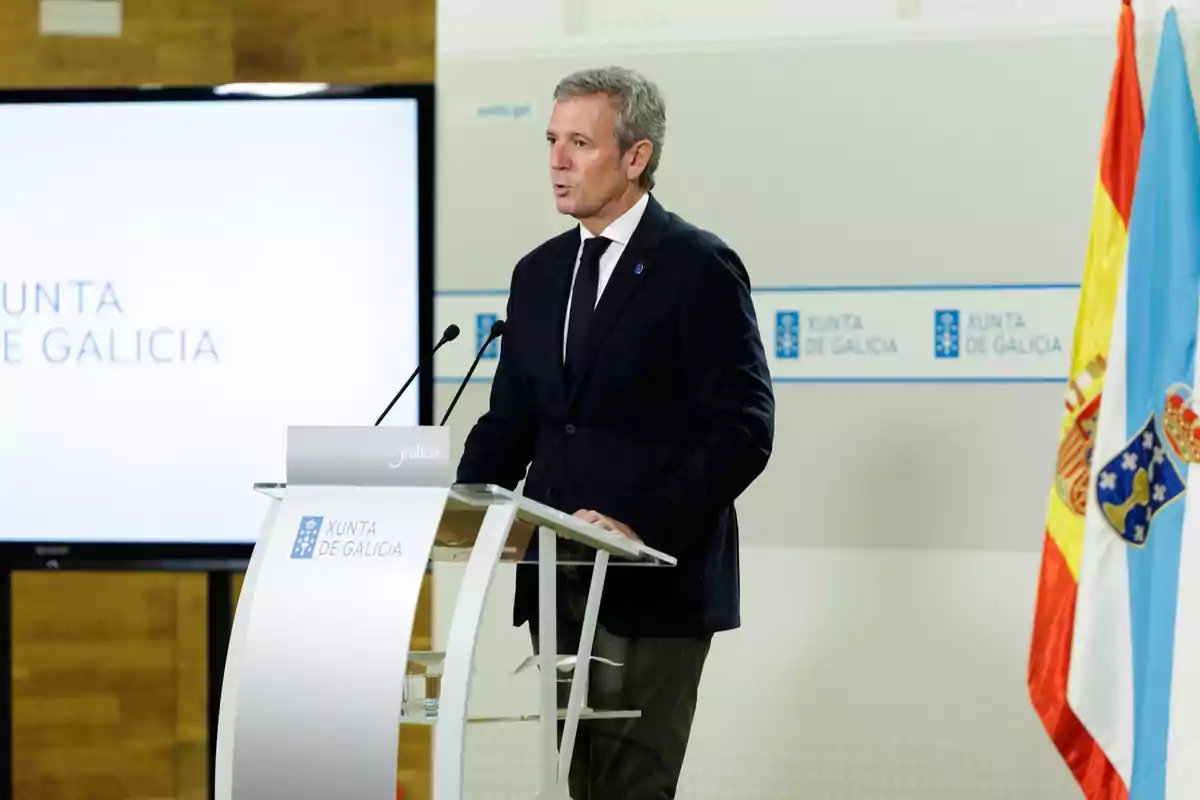 Hombre de traje oscuro hablando en un atril de la Xunta de Galicia con banderas oficiales al fondo
