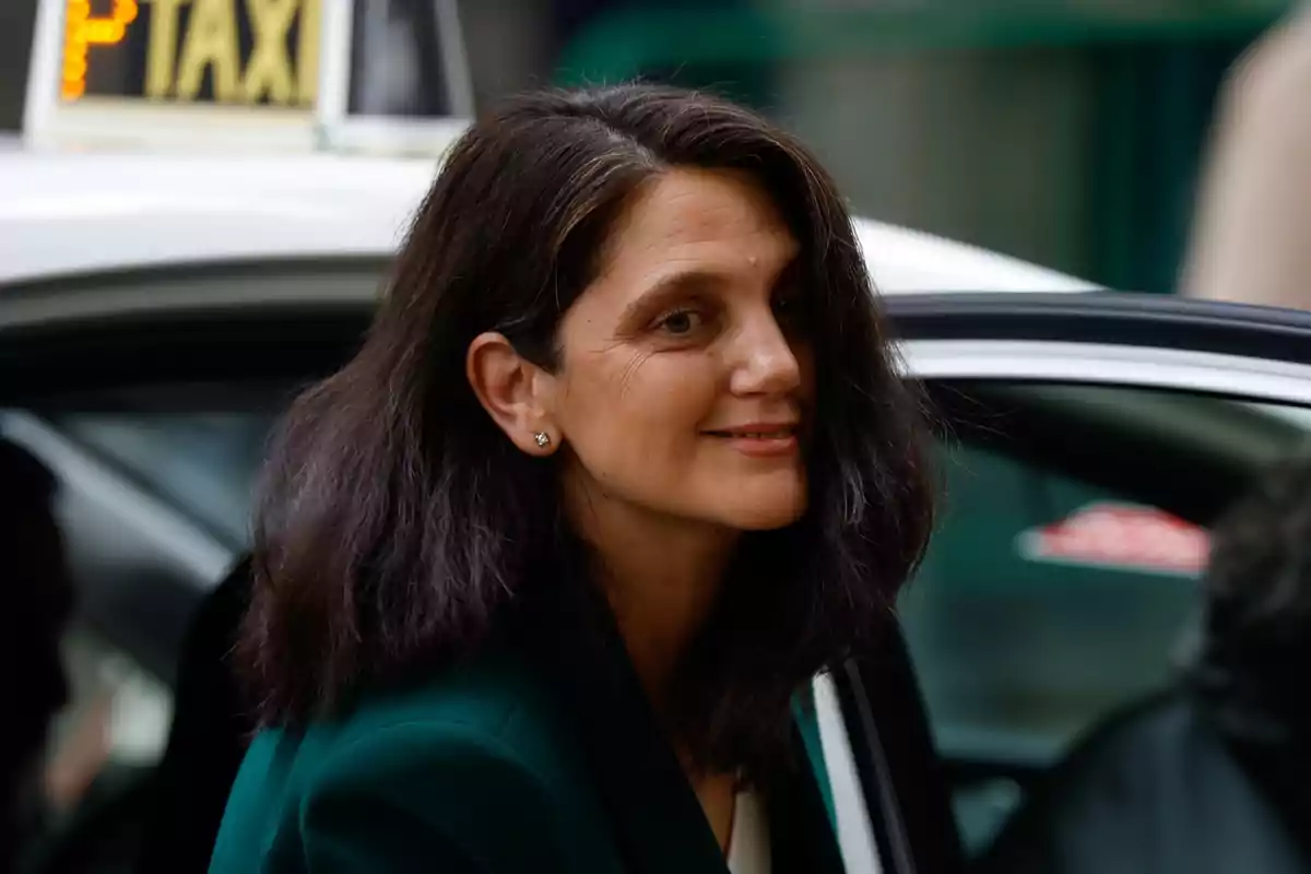 Mujer de cabello oscuro y suelto sonriendo mientras sale de un taxi