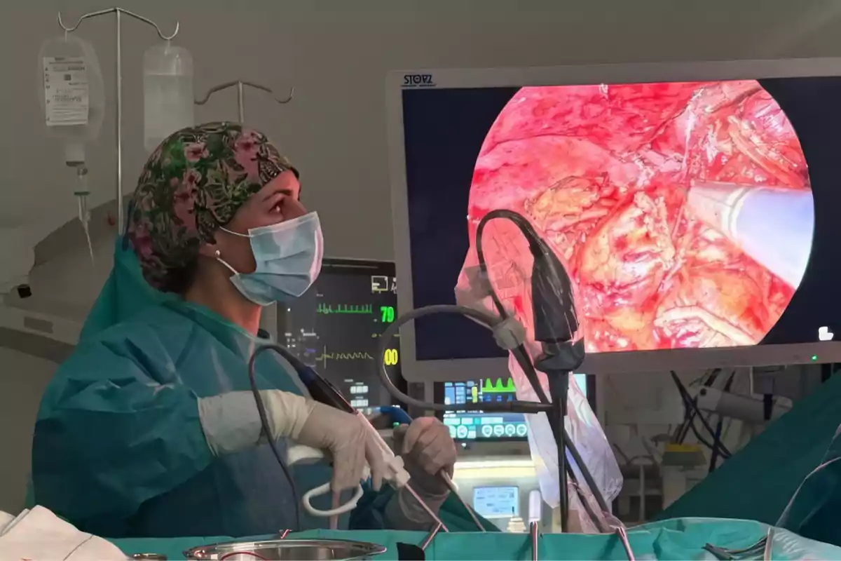 Cirujana con mascarilla y gorro quirúrgico observa un monitor que muestra una imagen endoscópica durante una operación en un quirófano