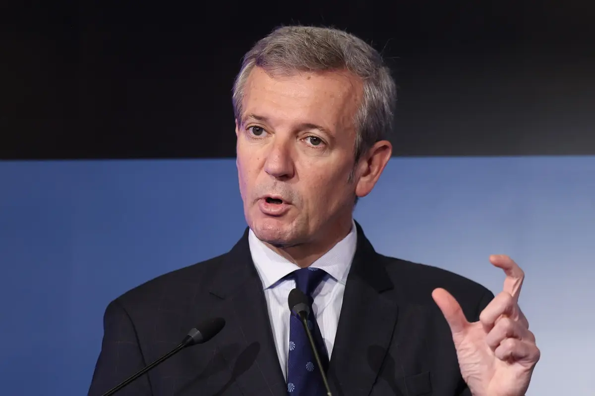 Hombre de cabello canoso con traje oscuro hablando frente a dos micrófonos y gesticulando con la mano