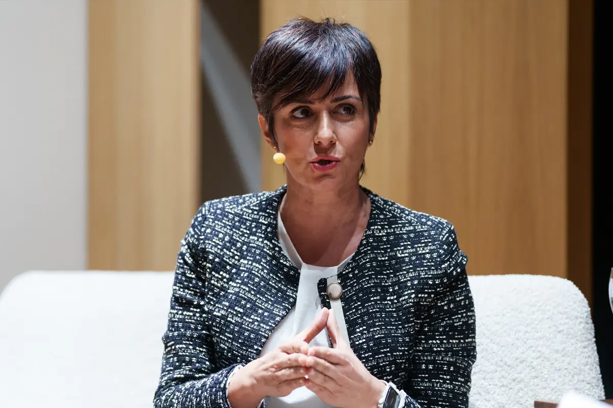 Mujer de cabello corto y oscuro hablando en un evento con micrófono de diadema y chaqueta formal