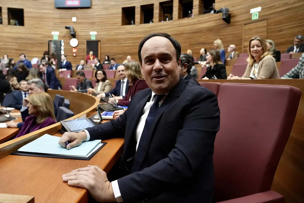 Hombre con traje oscuro sentado en un escaño de un parlamento rodeado de otras personas en una sala de sesiones