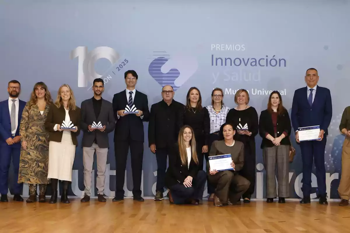 Grupo de personas posando en un escenario durante una ceremonia de premiación de innovación y salud, algunas sostienen trofeos y diplomas, todos vestidos de manera formal frente a un fondo azul con logotipos y texto del evento.