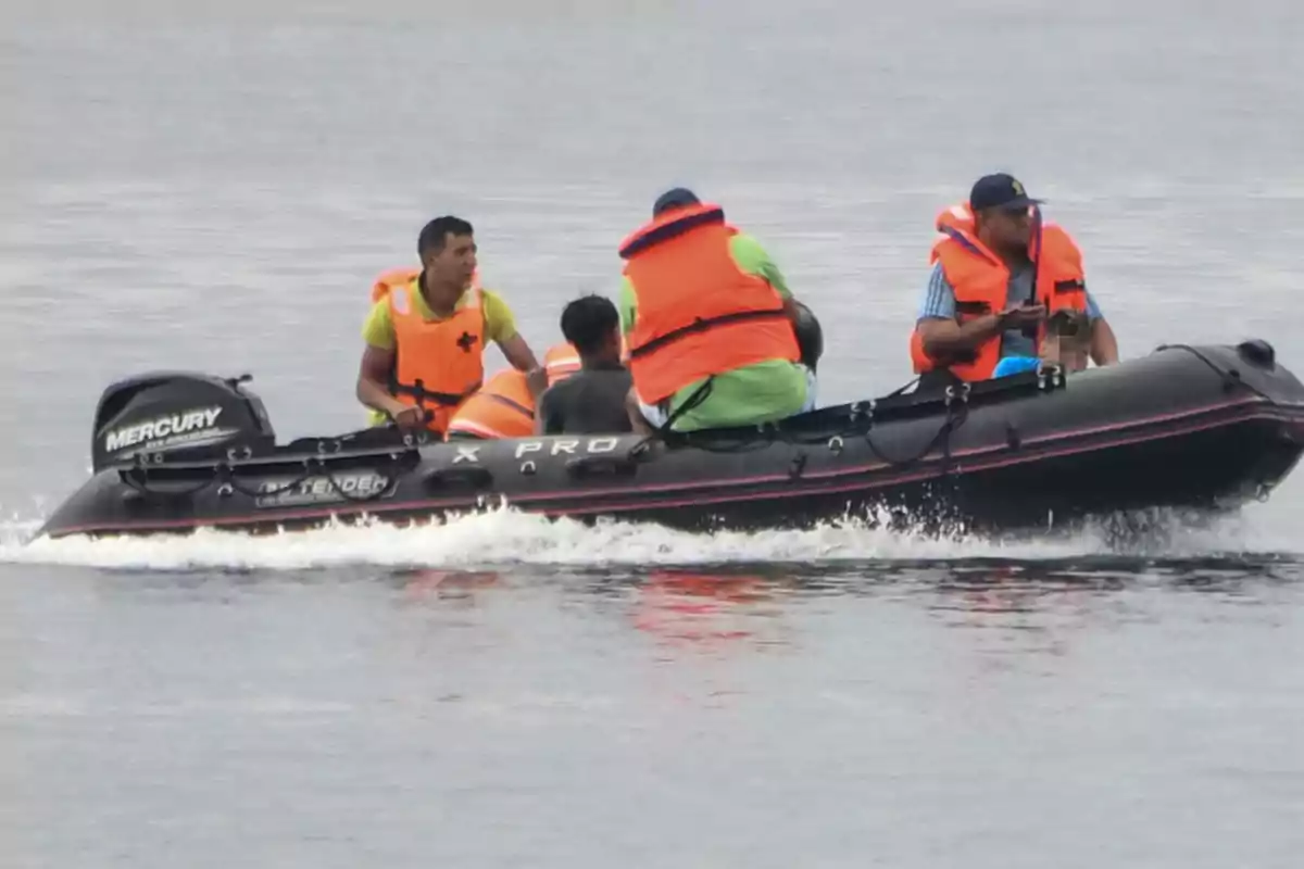 Varias personas con chalecos salvavidas naranjas viajan en una lancha inflable negra sobre el agua