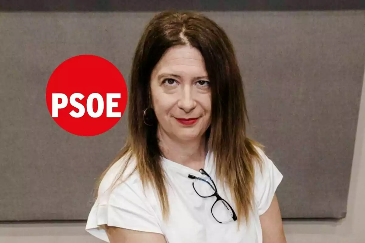 Mujer de cabello castaño y liso con gafas colgadas en la camiseta blanca, fondo gris y un círculo rojo con las letras PSOE a la izquierda