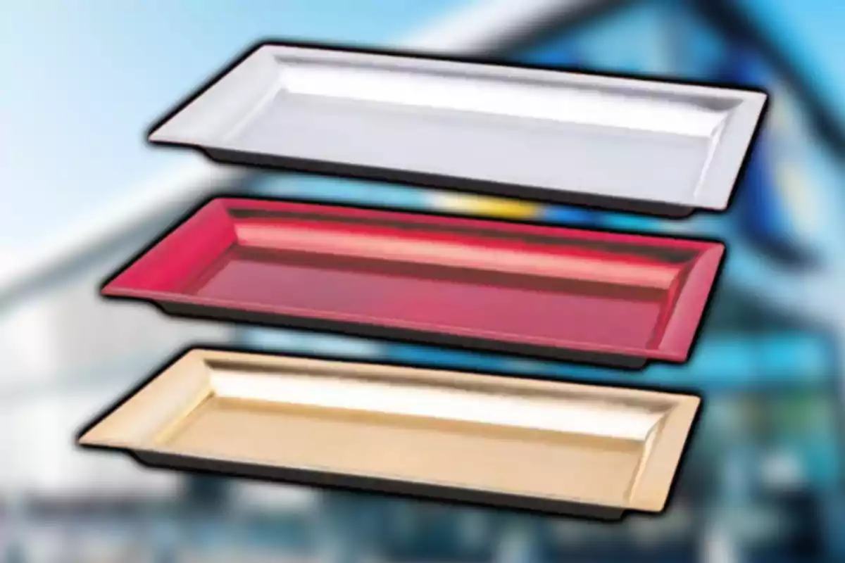 Tres charolas rectangulares de colores blanco, rojo y dorado sobre un fondo desenfocado.