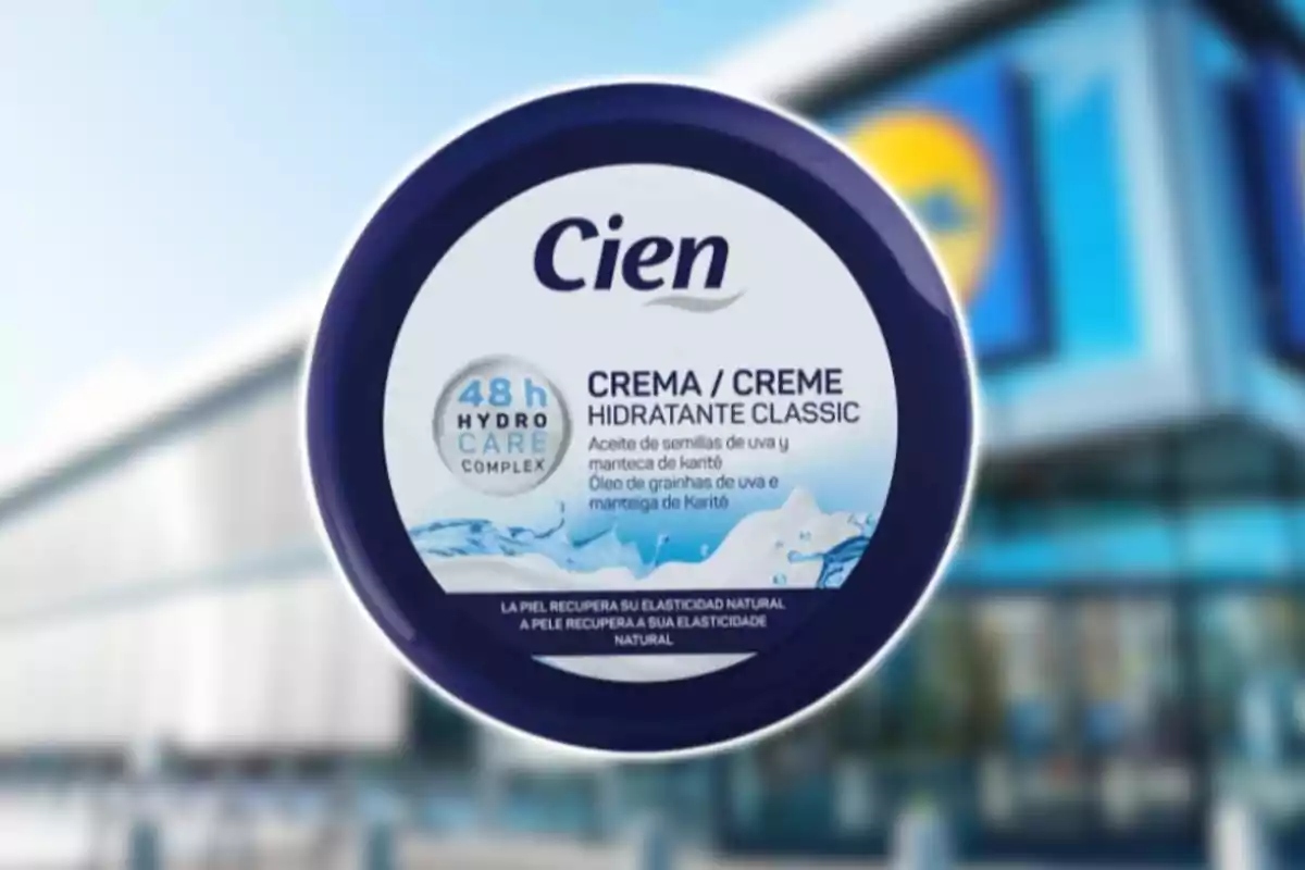 Envase redondo de crema hidratante Cien con tapa azul y etiqueta blanca, al fondo una tienda con fachada azul desenfocada.