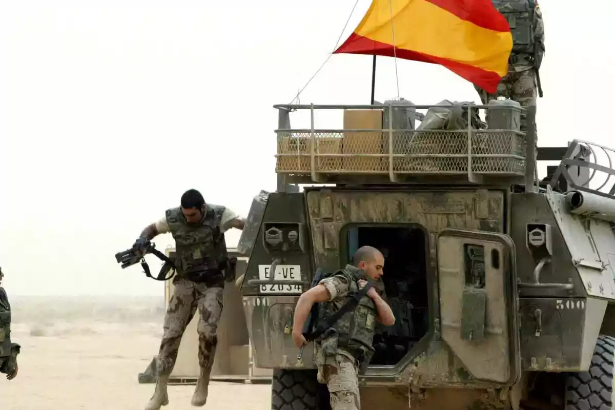 Soldados con uniforme militar bajando de un vehículo blindado en el desierto con una bandera de España ondeando en la parte superior del vehículo