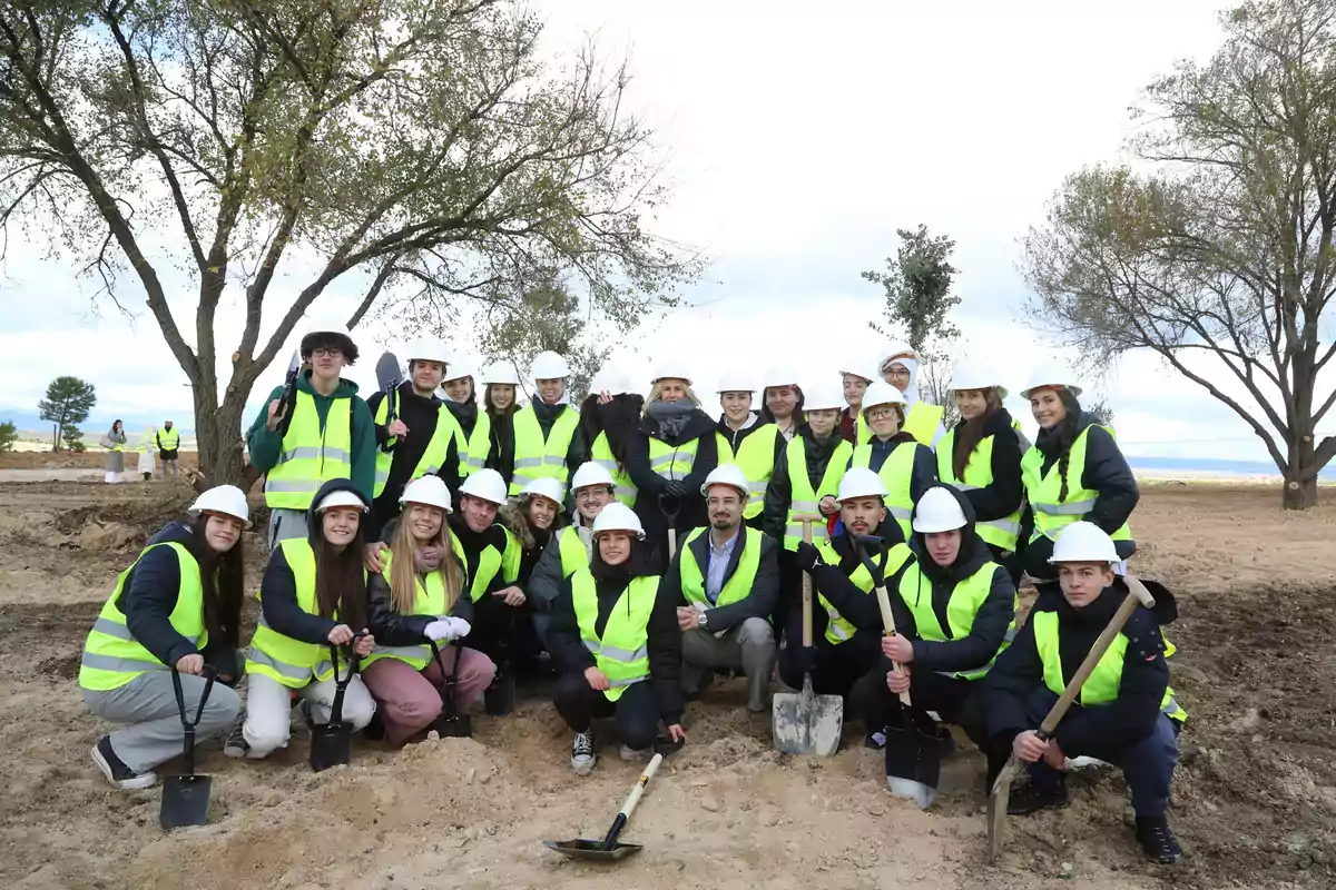 Grupo de personas con chalecos reflectantes y cascos blancos posando al aire libre en un terreno con palas y árboles al fondo