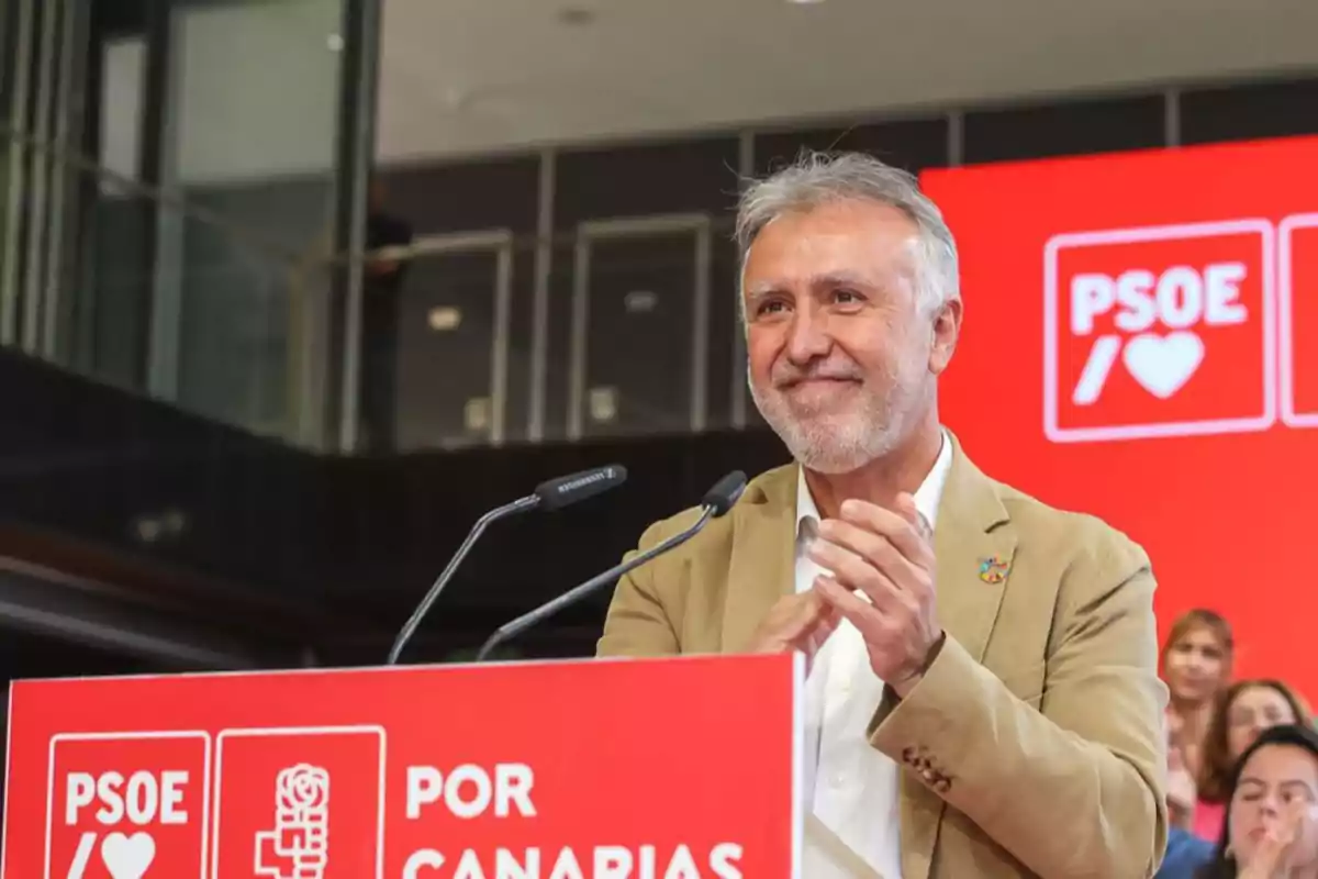 Ángel Víctor Torres aplaudiendo detrás de un atril rojo con el logo del PSOE y el texto Por Canarias en un evento político