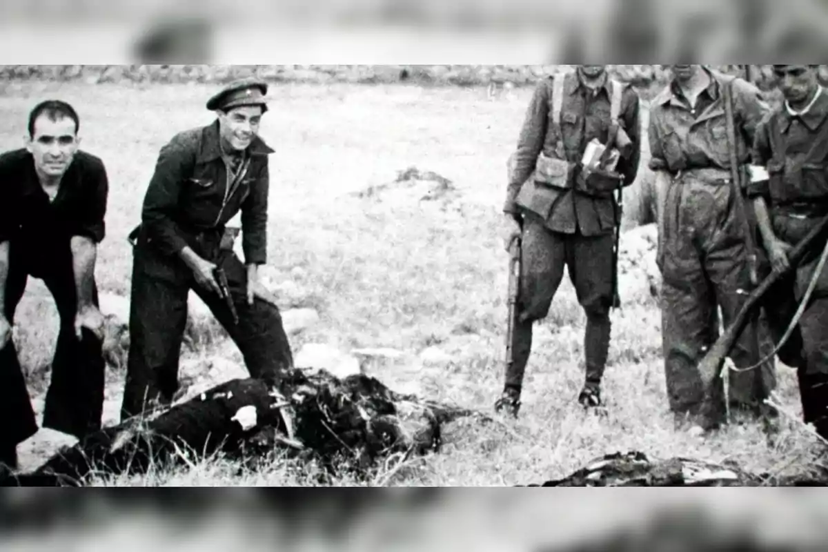 Varios hombres armados con uniforme militar posan junto a cuerpos en el suelo en un entorno al aire libre