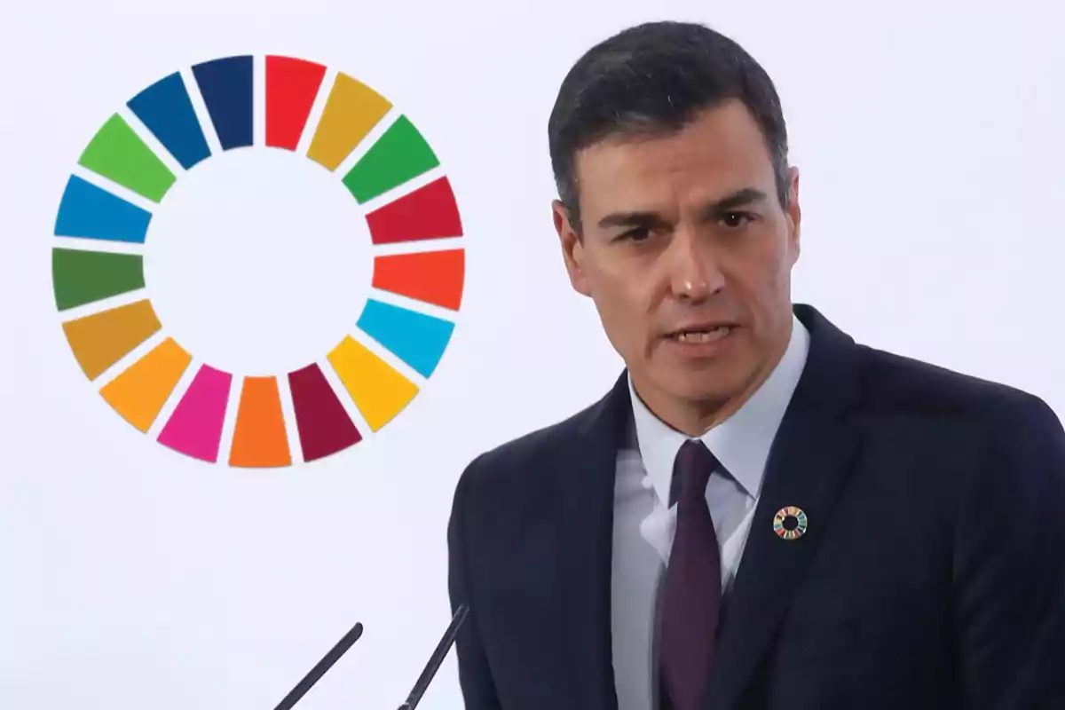 Hombre de traje oscuro hablando frente a un micrófono con el logo de los Objetivos de Desarrollo Sostenible al fondo