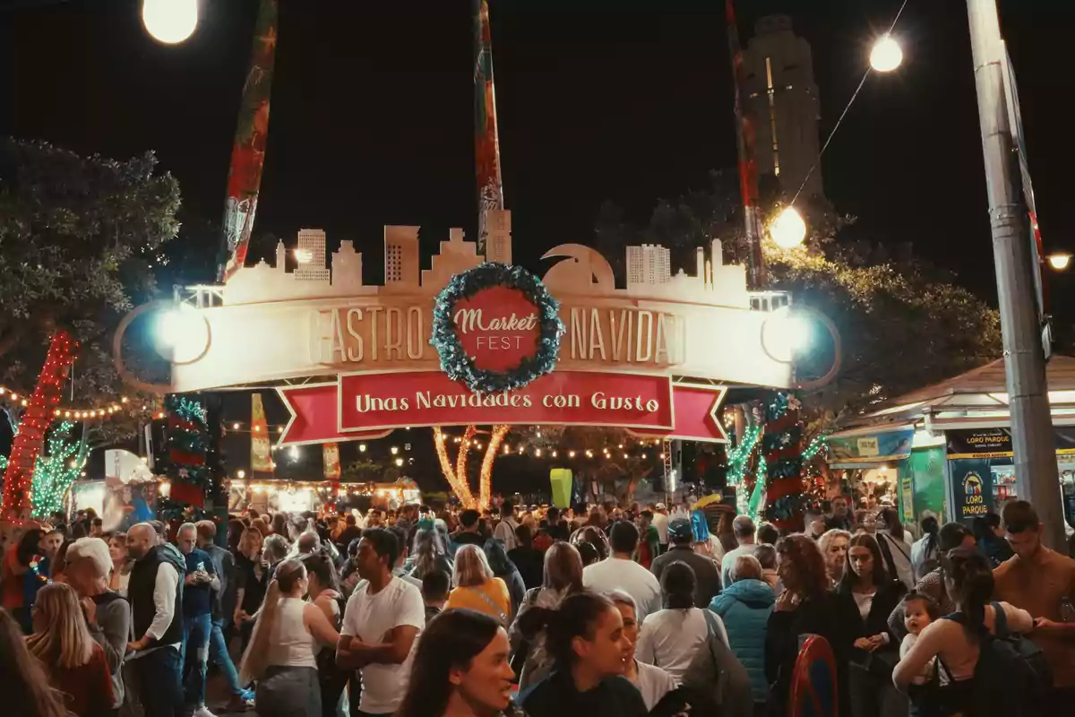 Multitud de personas disfrutando de un mercado navideño nocturno con luces y decoraciones festivas