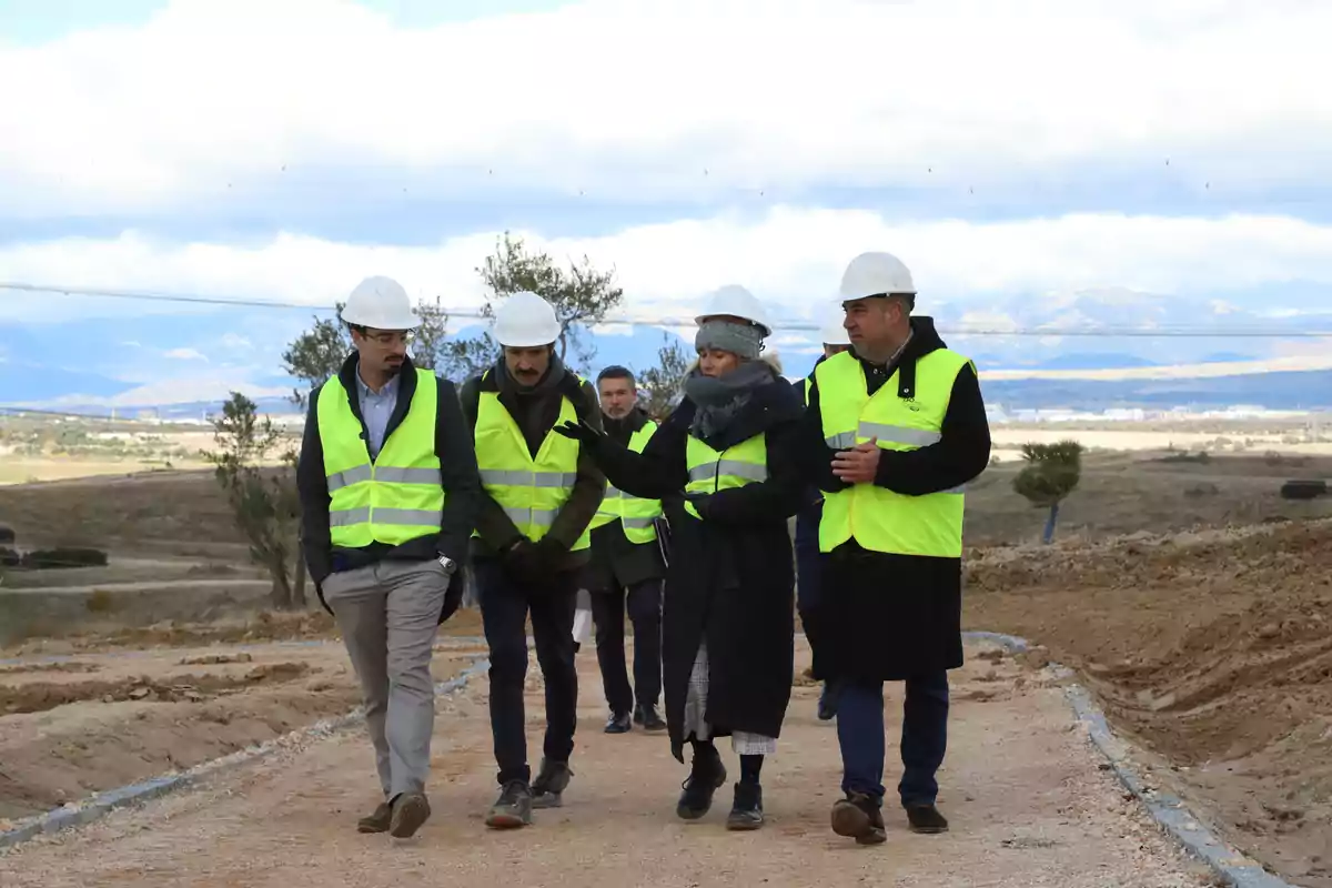 Grupo de personas con chalecos reflectantes y cascos blancos caminando por una obra en construcción al aire libre Grupo de personas con chalecos reflectantes y cascos blancos caminando por una obra en construcción al aire libre