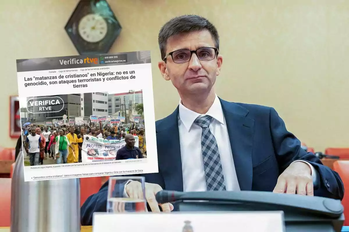 Un hombre con gafas y traje está sentado en una sala, mientras sostiene una imagen de una noticia sobre Nigeria y ataques terroristas, con una multitud protestando en la fotografía de la noticia.