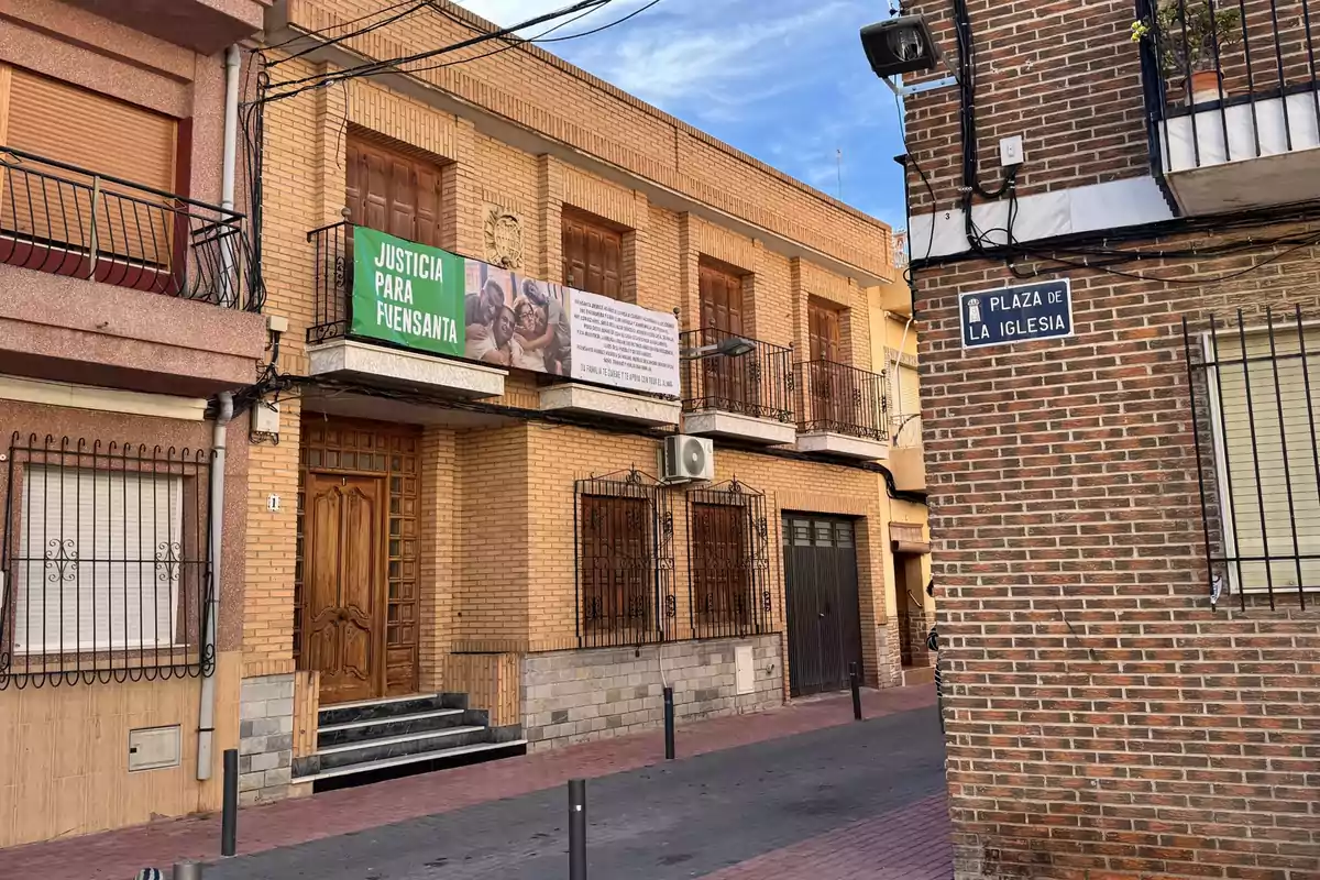 Fachada de edificio de ladrillo con pancartas en los balcones y un letrero que indica Plaza de la Iglesia en una esquina