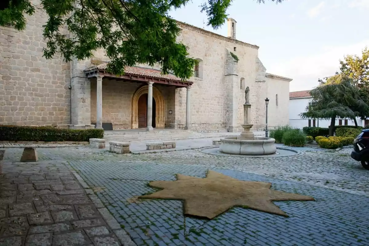 Iglesia de piedra con una fuente en el centro de una plaza empedrada y una estrella amarilla en el suelo Iglesia de piedra con una fuente en el centro de una plaza empedrada y una estrella amarilla en el suelo