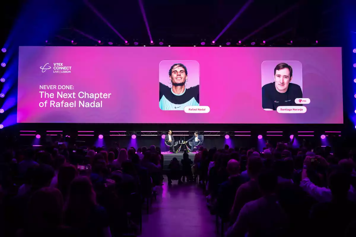 Auditorio lleno de personas observando una charla en un escenario iluminado con luces moradas, donde dos hombres conversan sentados bajo una pantalla gigante que muestra los nombres Rafael Nadal y Santiago Naranjo junto a sus fotografías y el título The Next Chapter of Rafael Nadal